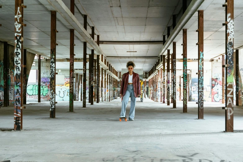 a man riding a skateboard on top of a cement floor, an album cover, by Nina Hamnett, pexels contest winner, graffiti, standing in a large empty hall, nathalie emmanuel, portrait full body, [[empty warehouse]] background