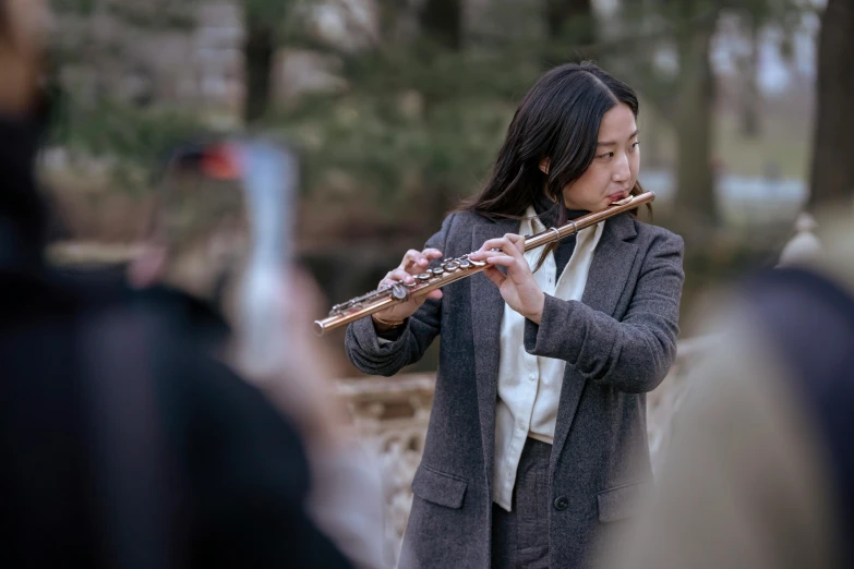 a woman playing a flute in front of a group of people, pexels contest winner, sydney park, fall season, asian human, holding a baguette