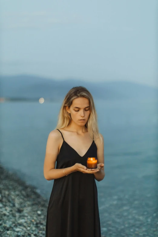 a woman standing on a beach holding an apple, by irakli nadar, pexels contest winner, candle lighting, portrait of sanna marin, medium format. soft light, holding a tangerine