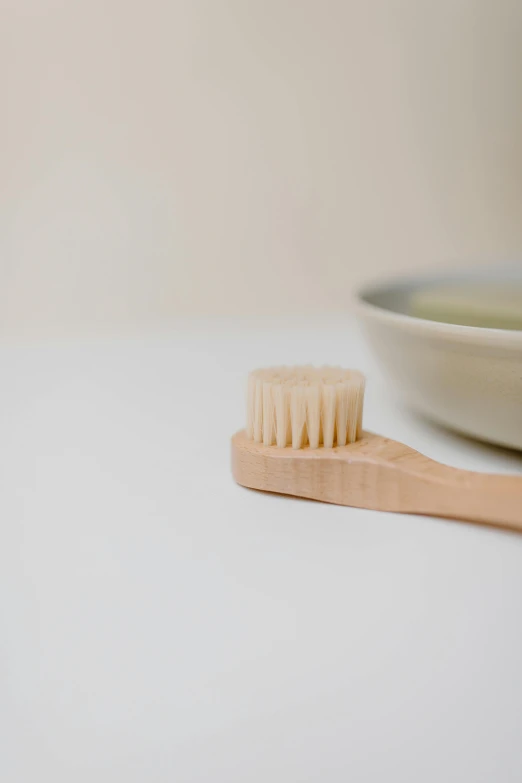 a wooden toothbrush sitting next to a bowl of toothpaste, unsplash, on a pale background, soup, stipple brush, natural skin