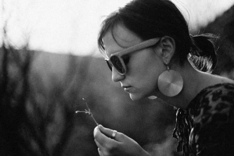 a black and white photo of a woman holding a flower, inspired by Sergio Larraín, sun glasses, christina ricci, earings, wooden jewerly