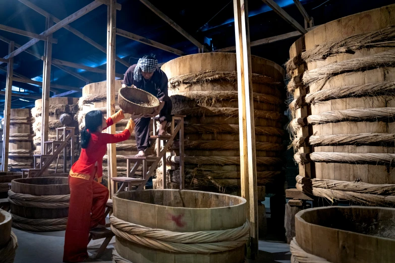 a woman that is standing in front of a bunch of barrels, inspired by Li Di, process art, made of bamboo, ao dai, mill, thumbnail