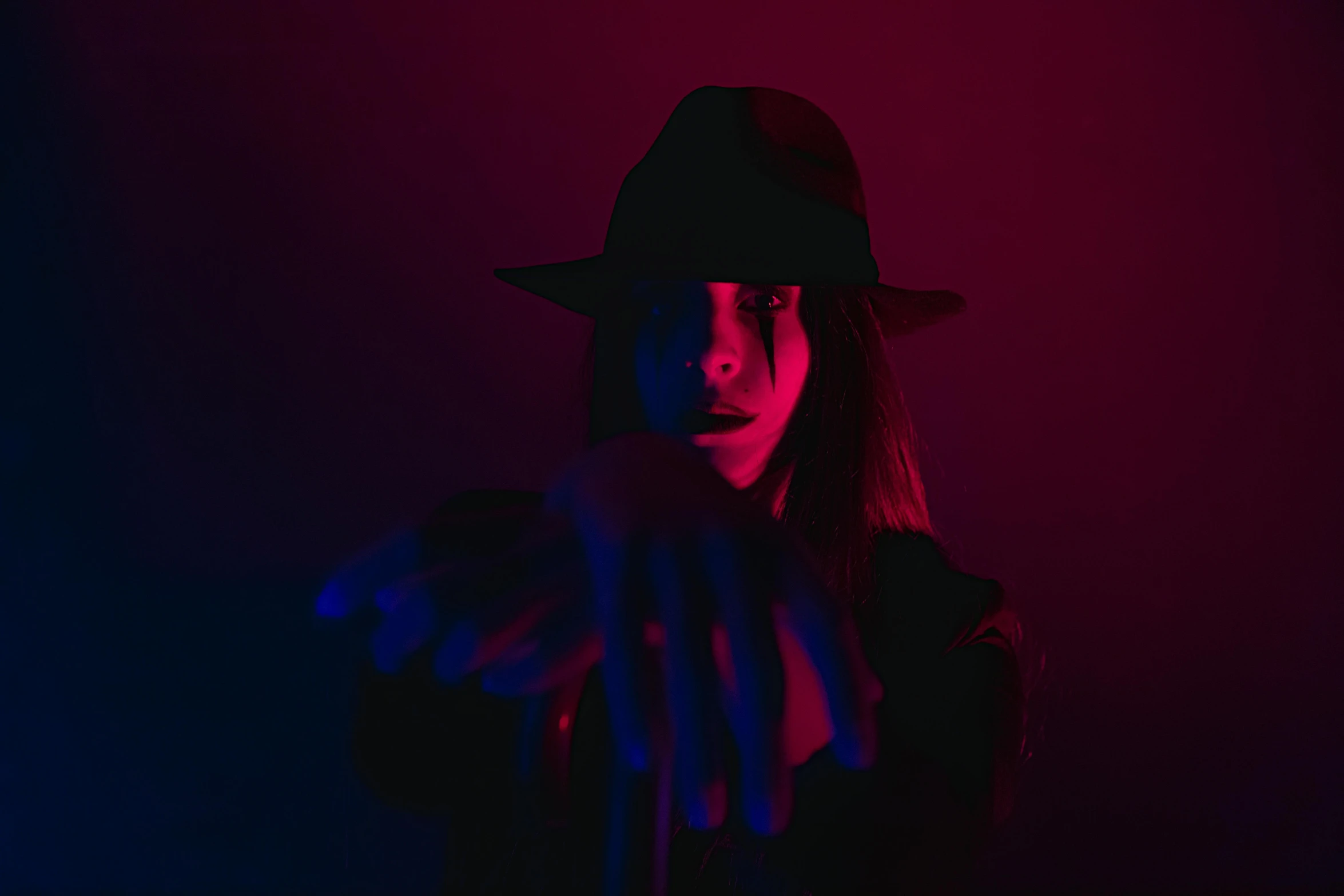 a woman wearing a hat standing in front of a red and blue light, pexels contest winner, threatening pose, androgynous vampire, faceless people dark, glowing hands