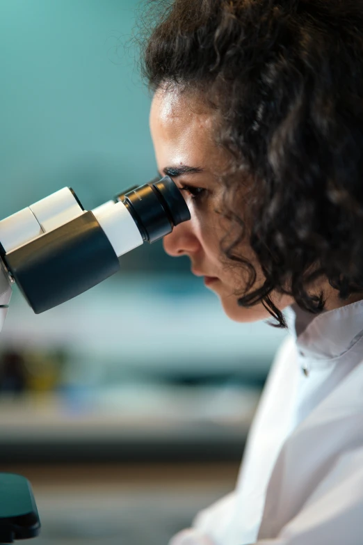 a woman in a lab coat looking through a microscope, a microscopic photo, shutterstock, jen atkin, hispanic, thirst, student