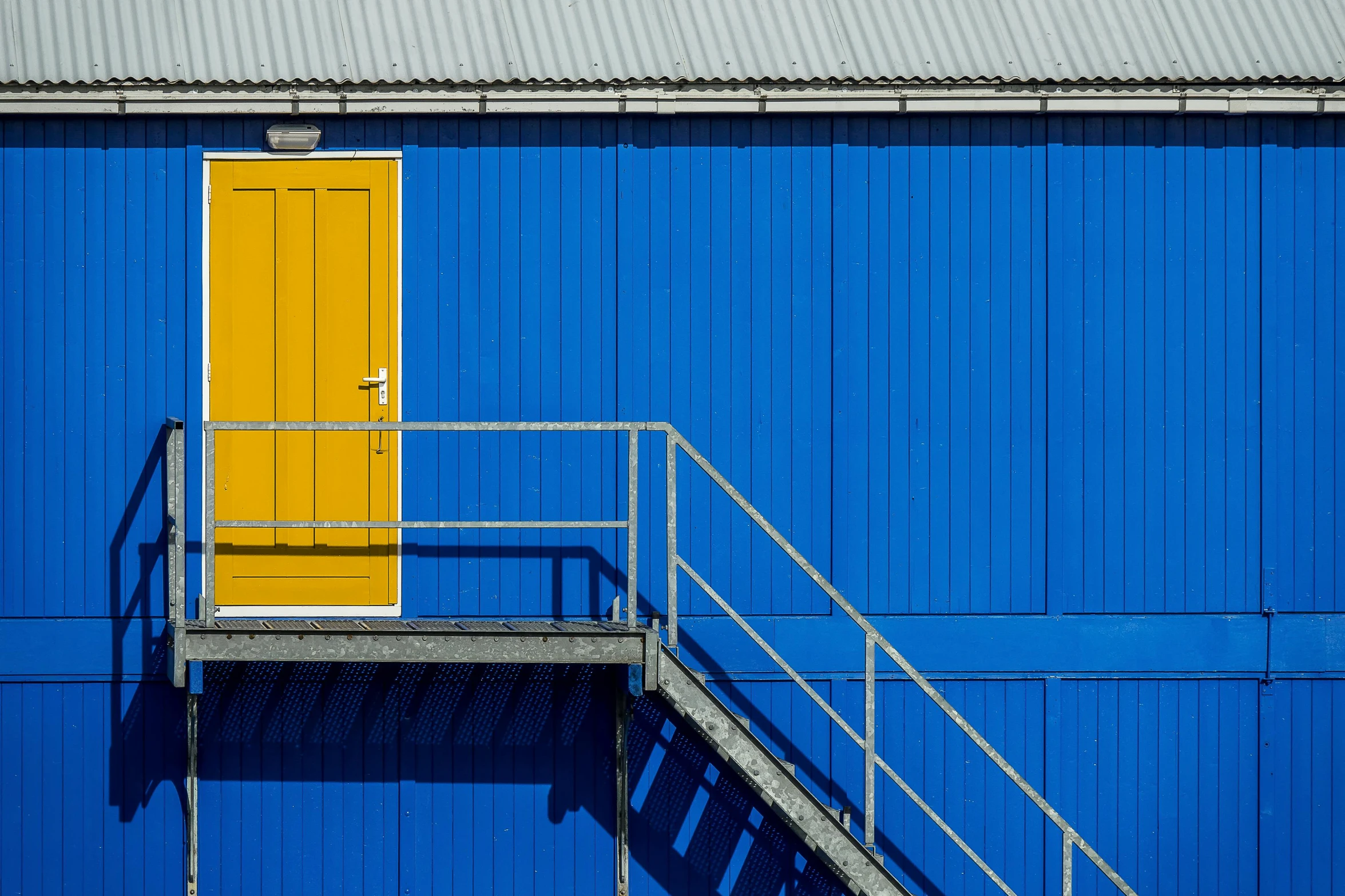 a blue building with a yellow door and stairs, by Sven Erixson, pexels contest winner, postminimalism, industrial colours, shed, shot on sony a 7, swedish style