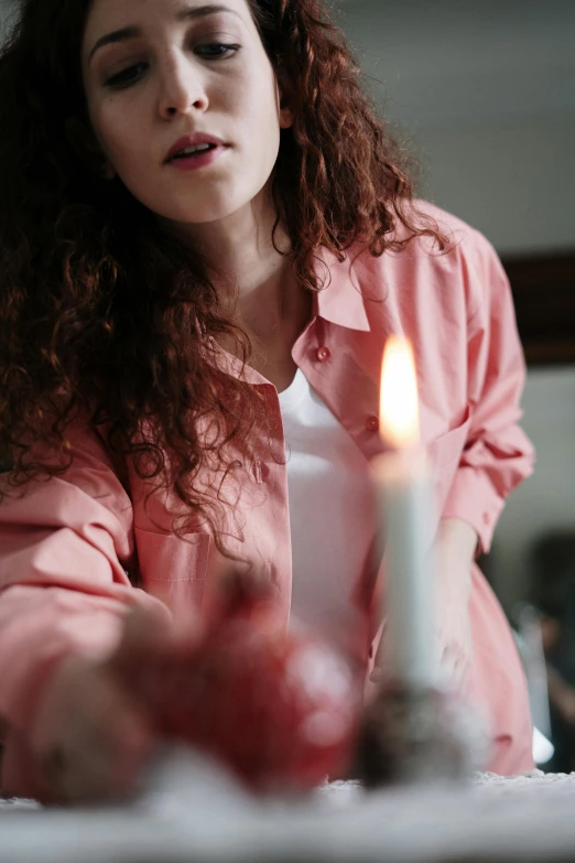 a woman sitting at a table with a lit candle, pexels, wearing a light shirt, walking down, a close up shot, pink
