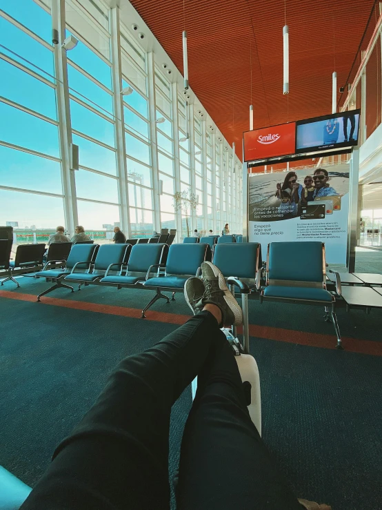 a person sitting in an airport waiting for their flight, by Emma Andijewska, pexels contest winner, photo of the cinema screen, blue sky, lying down, teenager hangout spot