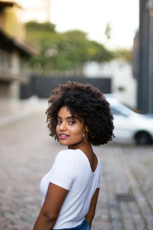 a beautiful young woman standing on a cobblestone street, by Lily Delissa Joseph, pexels contest winner, natural hair, in sao paulo, big hair, clean perfect symmetrical face