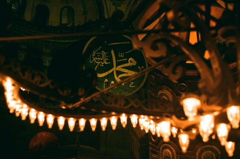 a close up of a chandelier with a clock in the background, hurufiyya, in dark robes with gold accents, caligraphy, on a canva, mosque interior