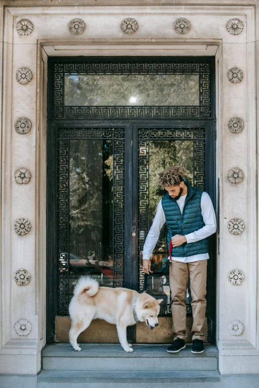 a man standing in front of a door with a dog, on the sidewalk, tan vest, classic vibes, stately
