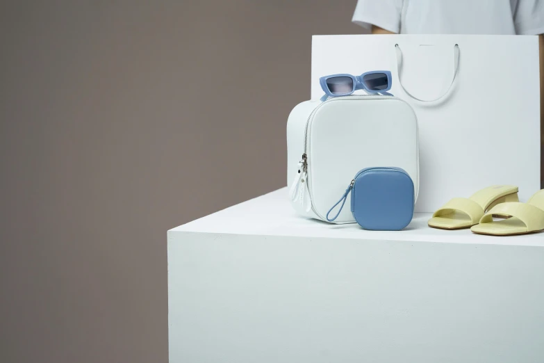 a couple of bags sitting on top of a white table, a still life, inspired by Bauhaus, bauhaus, wearing square glasses, pale blue, product showcase, sleek white
