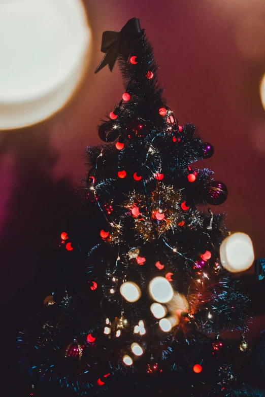 a small christmas tree with lights in the background, by Julia Pishtar, pexels, black and red color scheme, multiple stories, hazy, low - angle shot