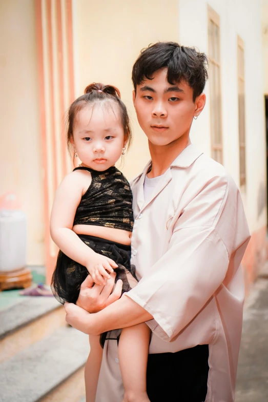 a man holding a baby in his arms, a picture, pexels contest winner, ao dai, with a kid, complex background, he is about 20 years old | short