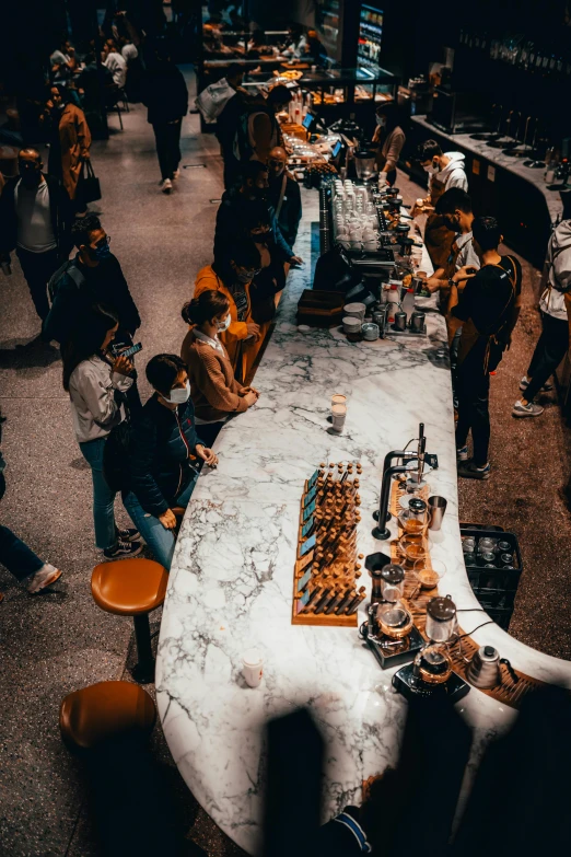 a group of people standing around a long table, by Daniel Lieske, trending on pexels, latte art, candy shop in a mall, thumbnail, busy night