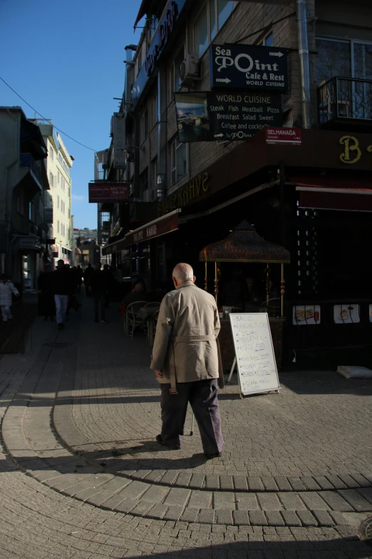 a man walking down a street next to tall buildings, an album cover, inspired by Nadim Karam, renaissance, old shops, istanbul, midday photograph, an elderly