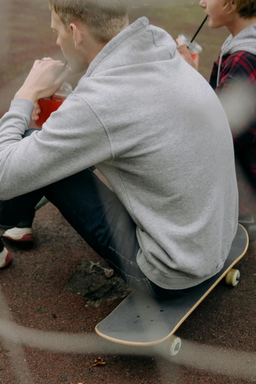 a couple of people sitting on top of a skateboard, grey sweater, over his shoulder, head down, half image