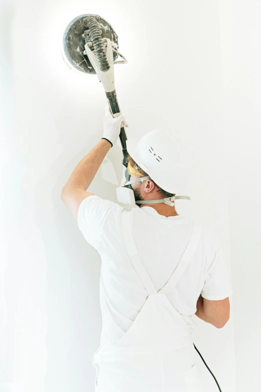 a man that is standing up with a tennis racket, painting on the ceiling, hard hat, cool white color temperature, before a stucco wall