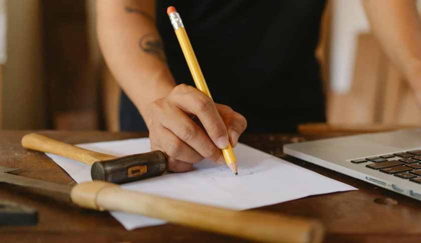 a person writing on a piece of paper with a pencil, a drawing, pexels contest winner, holding a wooden staff, carpenter, indi creates, tabletop