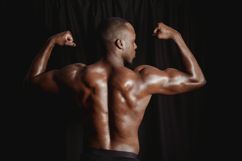 a man flexing his muscles in front of a black background, by Sam Charles, pexels contest winner, back to back, ebony skin, arched back, various posed