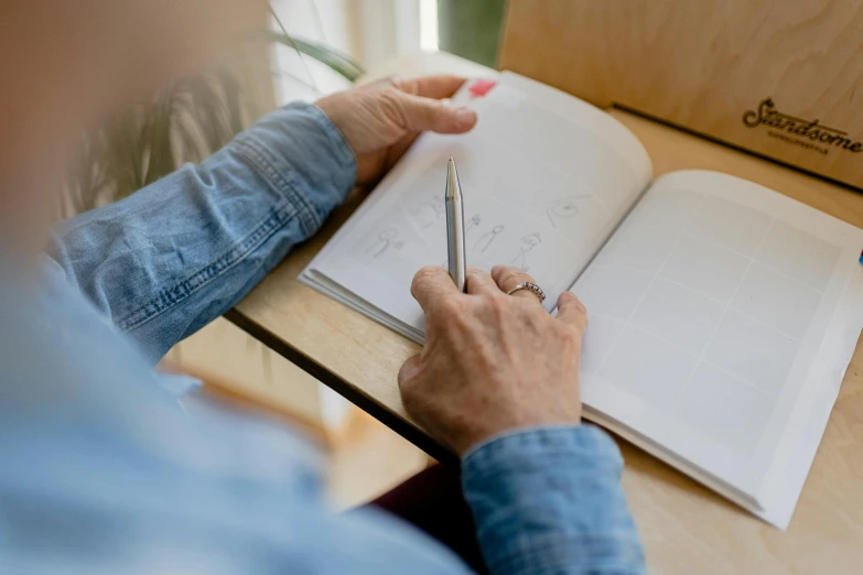 a person sitting at a table writing in a book, a drawing, by Carey Morris, pexels contest winner, whiteboards, high angle shot, thumbnail, background image