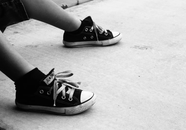 a black and white photo of a person sitting on a skateboard, a black and white photo, by Lucia Peka, pexels, running shoes, innocence, converse, my little everything