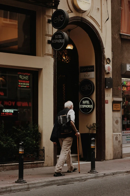 a man walking down a street next to a tall building, a photo, pexels contest winner, art nouveau, white-haired, gothic quarter, exiting store, hiking cane