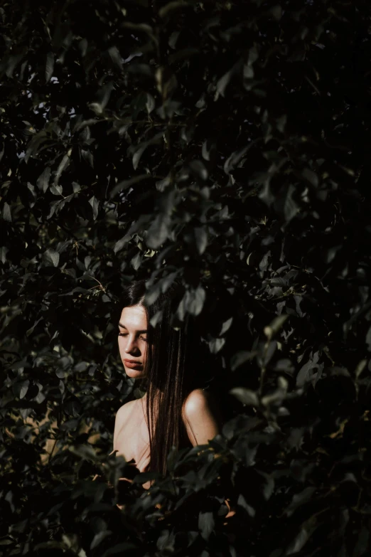 a woman standing in the middle of a lush green forest, inspired by Elsa Bleda, on black background, with ivy, brunette woman, hides in the shadows of trees