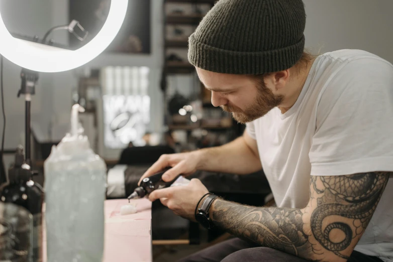 a man that is sitting down with a camera, an airbrush painting, trending on pexels, tattoo parlor photo, avatar image, crafting, delicate and precise brushwork