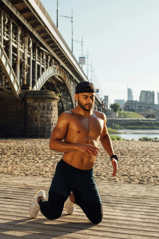 a man running on a beach next to a bridge, with abs, in london, athletic crossfit build, brown