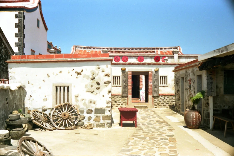 a stone building with a bench in front of it, inspired by Carlos Francisco Chang Marín, mingei, white buildings with red roofs, xianxia, 2 0 0 0's photo, small port village