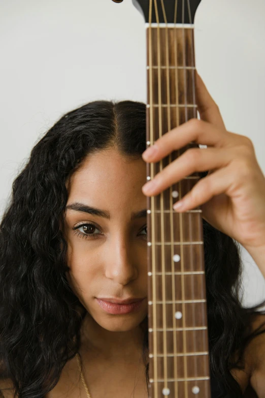 a woman holding a guitar in front of her face, medium skin tone, young middle eastern woman, 2019 trending photo, looking partly to the left
