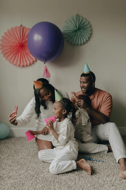 a couple of people that are sitting on the floor, inspired by The Family Circus, pexels contest winner, party hats, portrait of family of three, ( ( dark skin ) ), taking selfies