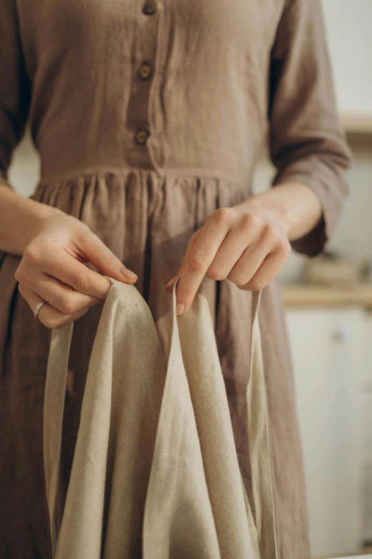 a woman in a brown dress holding a bag, by Grytė Pintukaitė, pexels contest winner, holding magical kitchen knives, ecru cloth, morning detail, wearing a long flowy fabric