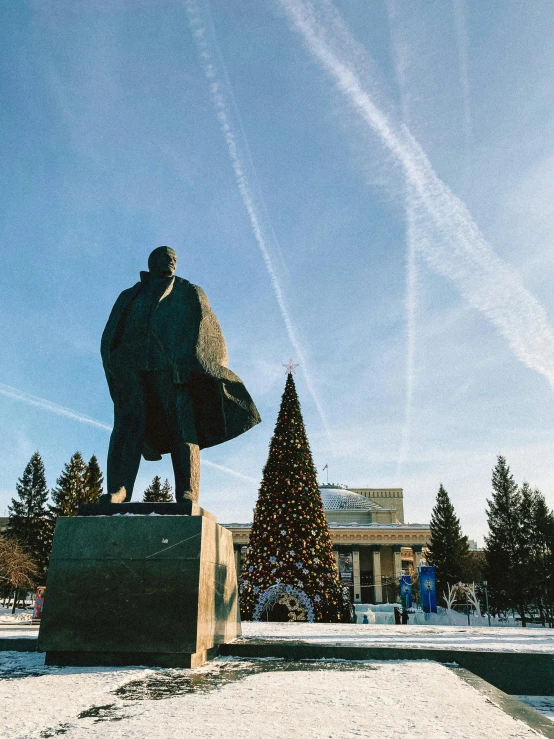 a statue of a man standing in front of a christmas tree, by Julia Pishtar, pexels contest winner, socialist realism, he wears a big coat, skies, yeltsin, university