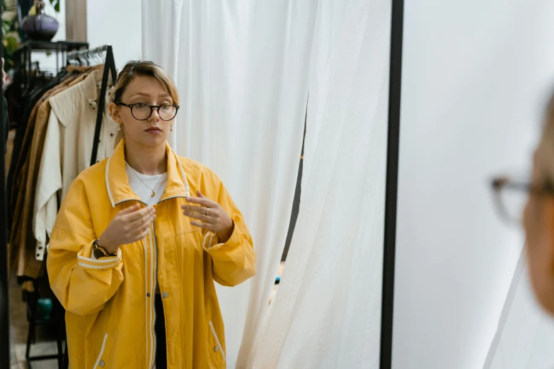 a woman in a yellow raincoat standing in front of a mirror, a hyperrealistic painting, trending on unsplash, standing in class, with a white background, performance art, wearing lab coat and glasses