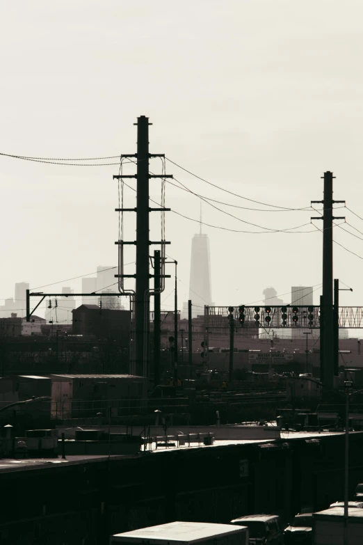 a black and white photo of a train yard, poster art, inspired by Elsa Bleda, tonalism, chicago skyline, power lines, pastel', view from a distance