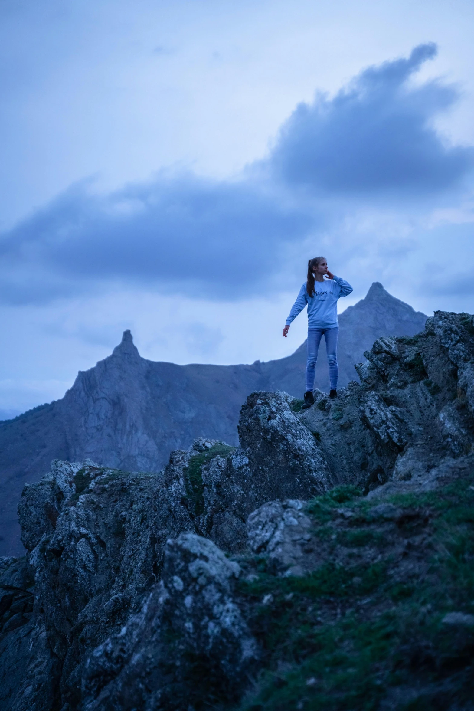 a woman standing on top of a rocky mountain, blue hour lighting, skye meaker, grey, devil's horns