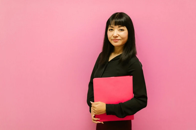 a woman standing in front of a pink wall holding a pink folder, inspired by Chizuko Yoshida, professional profile picture, gemma chan, profile image, professional profile photo