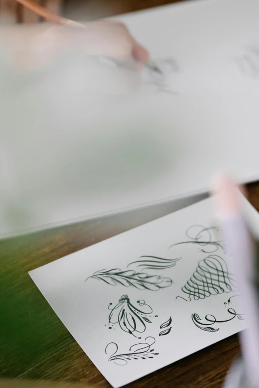 a person is drawing on a piece of paper, a drawing, by Jessie Algie, trending on pexels, intricate art deco leaf designs, blurry and dreamy illustration, on a table, seasonal