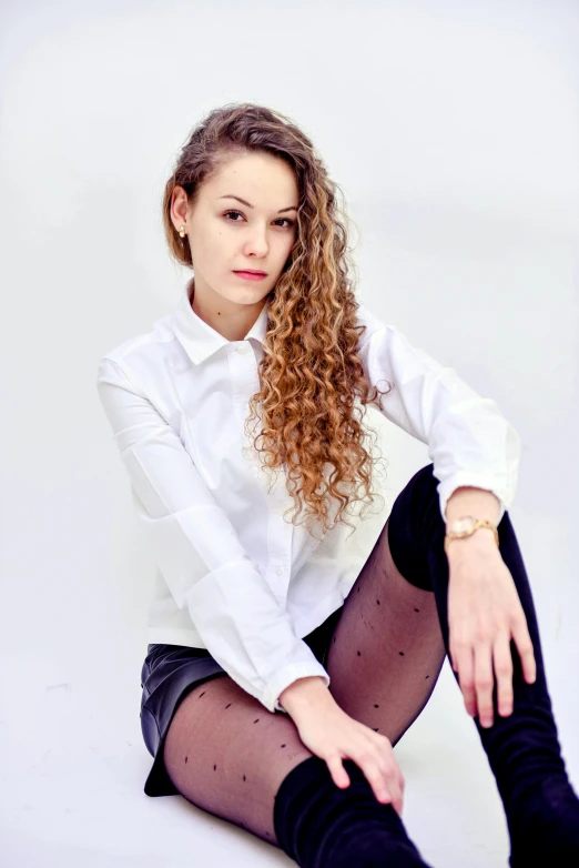 a woman sitting on the ground with her legs crossed, very very curly blond hair, wearing white tights, photo of džesika devic, 'white background'!!!