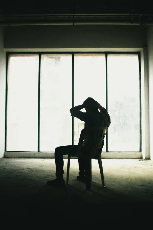 a person sitting in a chair in front of a window, pexels, devastated, single silhouette figure, hugging his knees, in a room