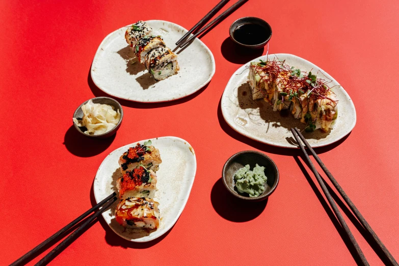 a red table topped with plates of food and chopsticks, unsplash, mingei, california roll, four hands, jen atkin, sky line