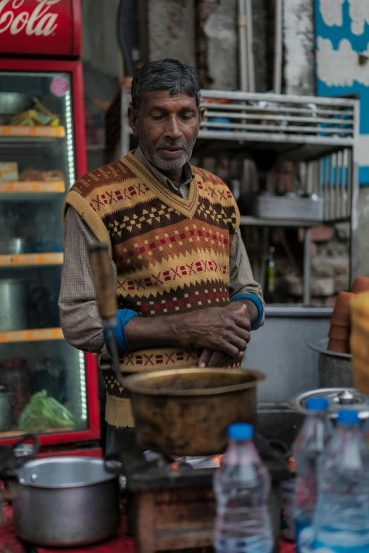 a man standing in front of a store filled with food, a portrait, inspired by Steve McCurry, trending on unsplash, moroccan tea set, ethiopian, he is wearing a brown sweater, old charismatic mechanic