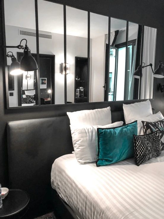 a bed room with a neatly made bed and a large mirror, by Robbie Trevino, pexels contest winner, art nouveau, black and cyan color scheme, paris hotel style, lights inside, white and teal metallic accents