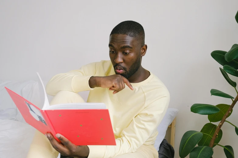 a man sitting on a bed reading a book, pexels contest winner, happening, wearing red and yellow clothes, mkbhd, avatar image, silly and serious