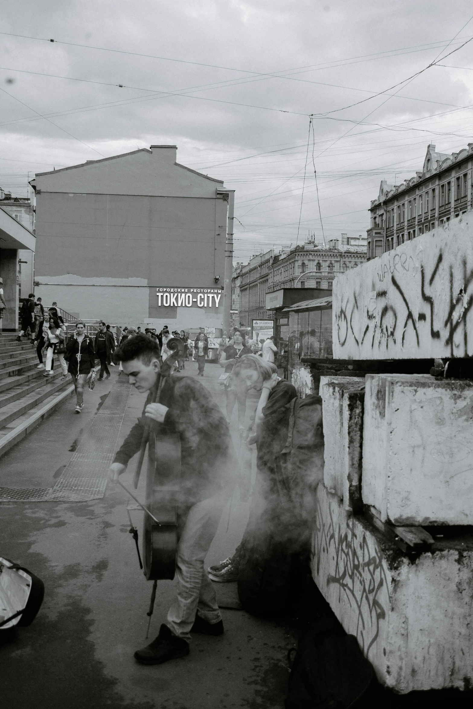 a black and white photo of a man walking down a street, a black and white photo, by Tamas Galambos, reddit, graffiti, crowded square, coming down the stairs, helsinki, mist below buildings