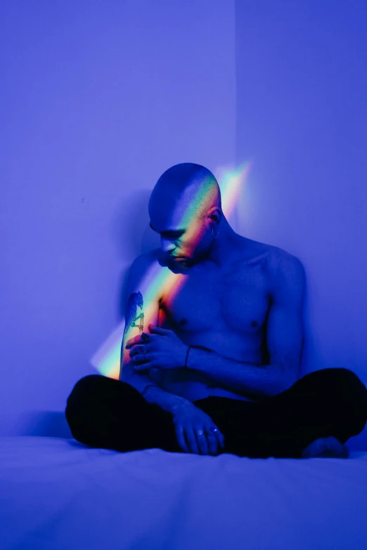 a man sitting on a bed looking at his phone, an album cover, pexels contest winner, holography, muscular bald man, volumetric rainbow lighting, man with a blue heart, chakras