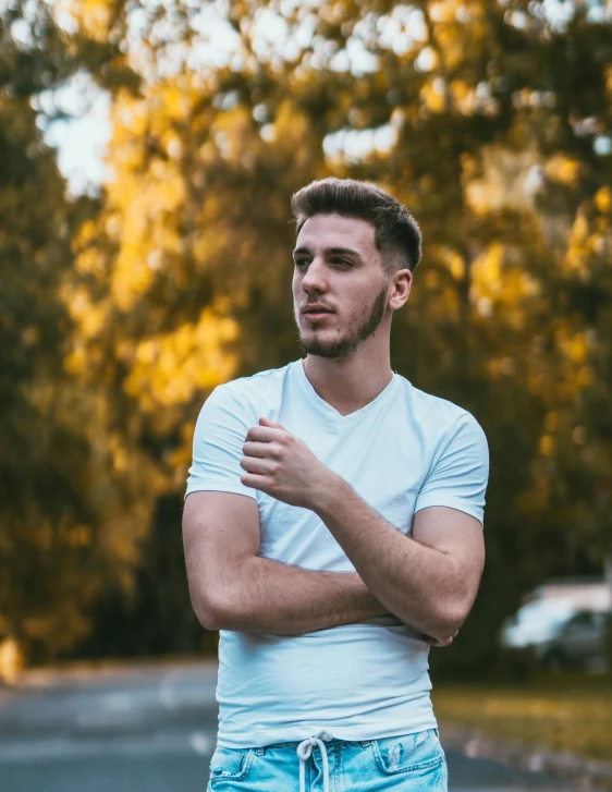 a man standing on the side of a road with his arms crossed, trending on pexels, non binary model, short stubble, in a park, mark edward fischbach