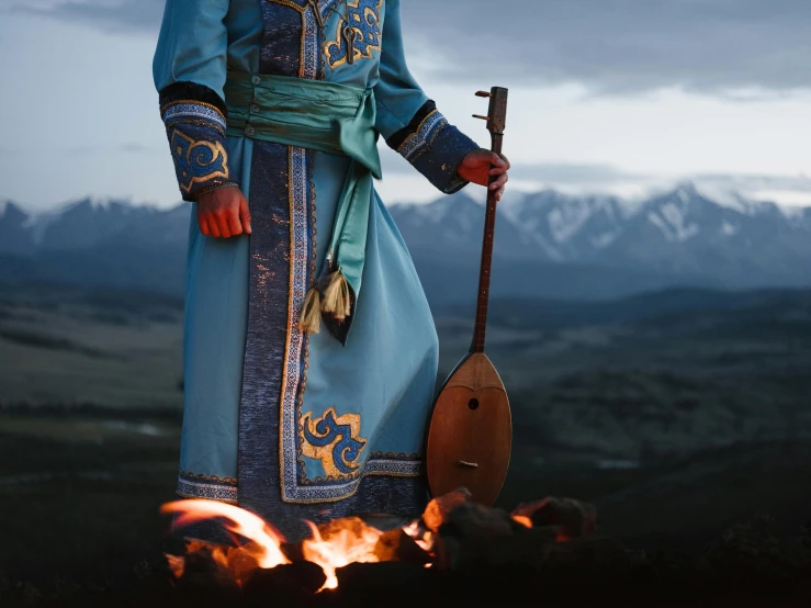 a man that is standing in front of a fire, an album cover, pexels contest winner, hurufiyya, traditional costume, mongol, blue, lute