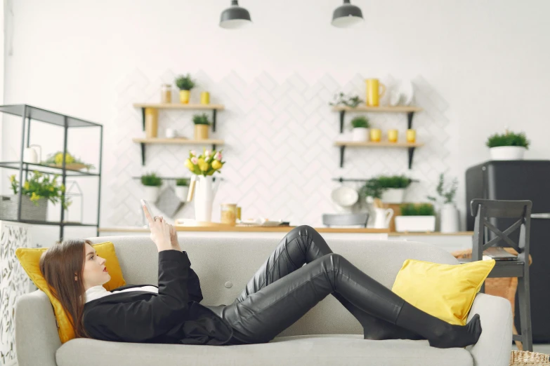 a woman laying on a couch reading a book, a cartoon, trending on pexels, yellow and charcoal leather, leather pants, androgynous person, looking at his phone